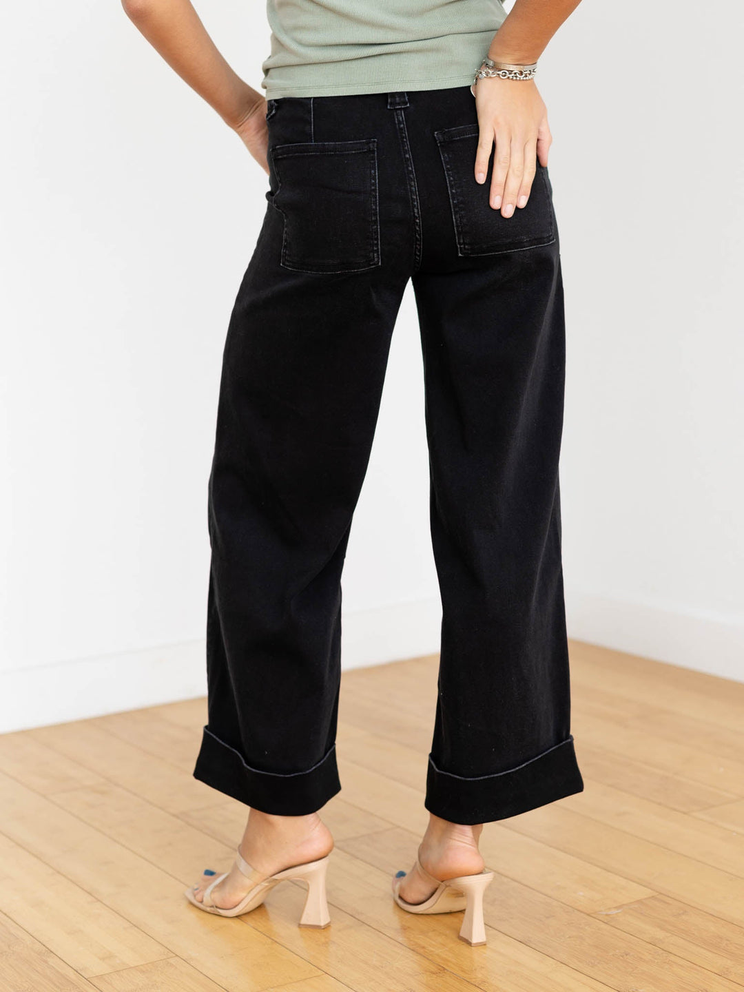 Person wearing black wide-leg jeans on a wooden floor with a white wall background