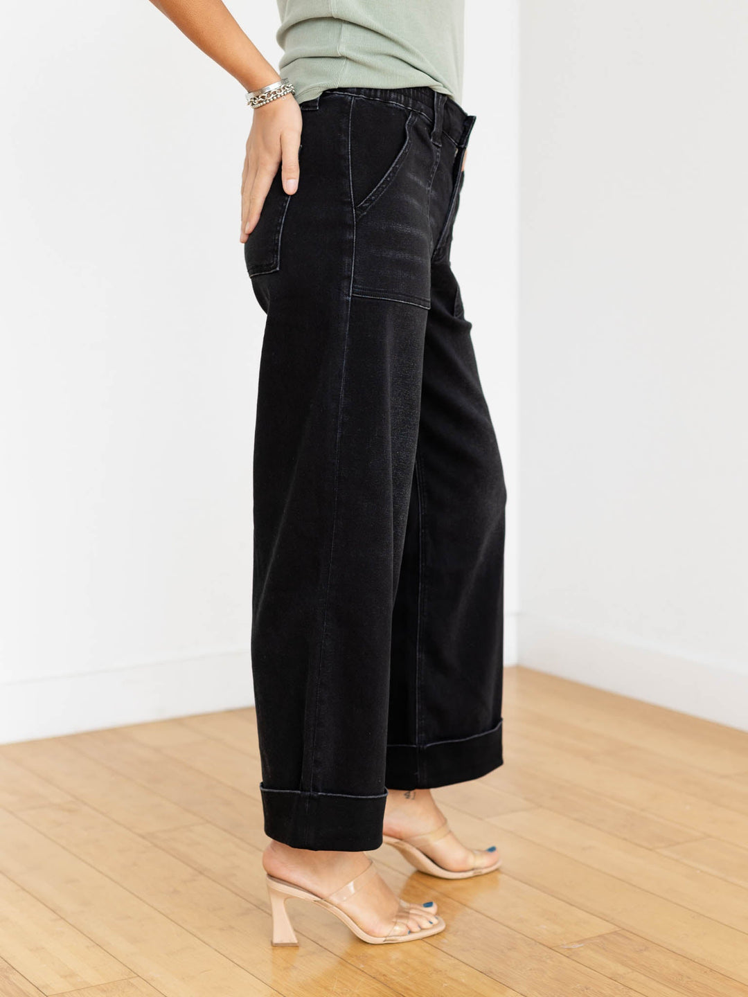Person wearing black wide-leg pants and a green top on a wooden floor.