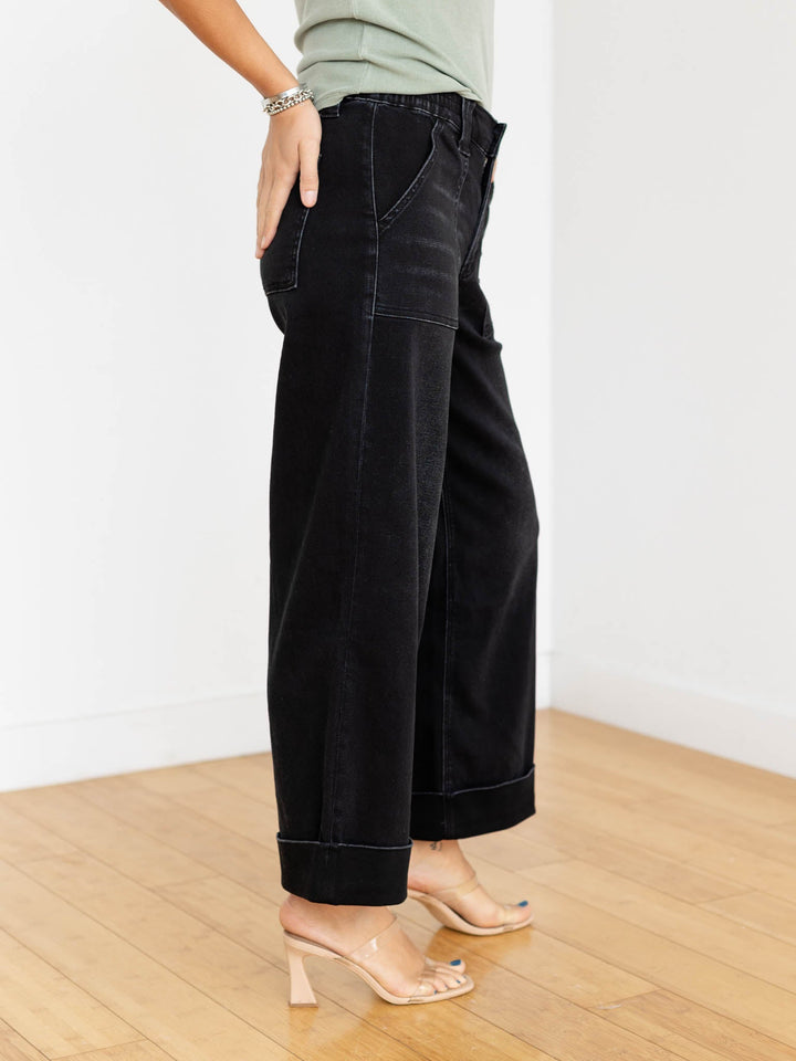 Person wearing black wide-leg pants and a green top on a wooden floor.