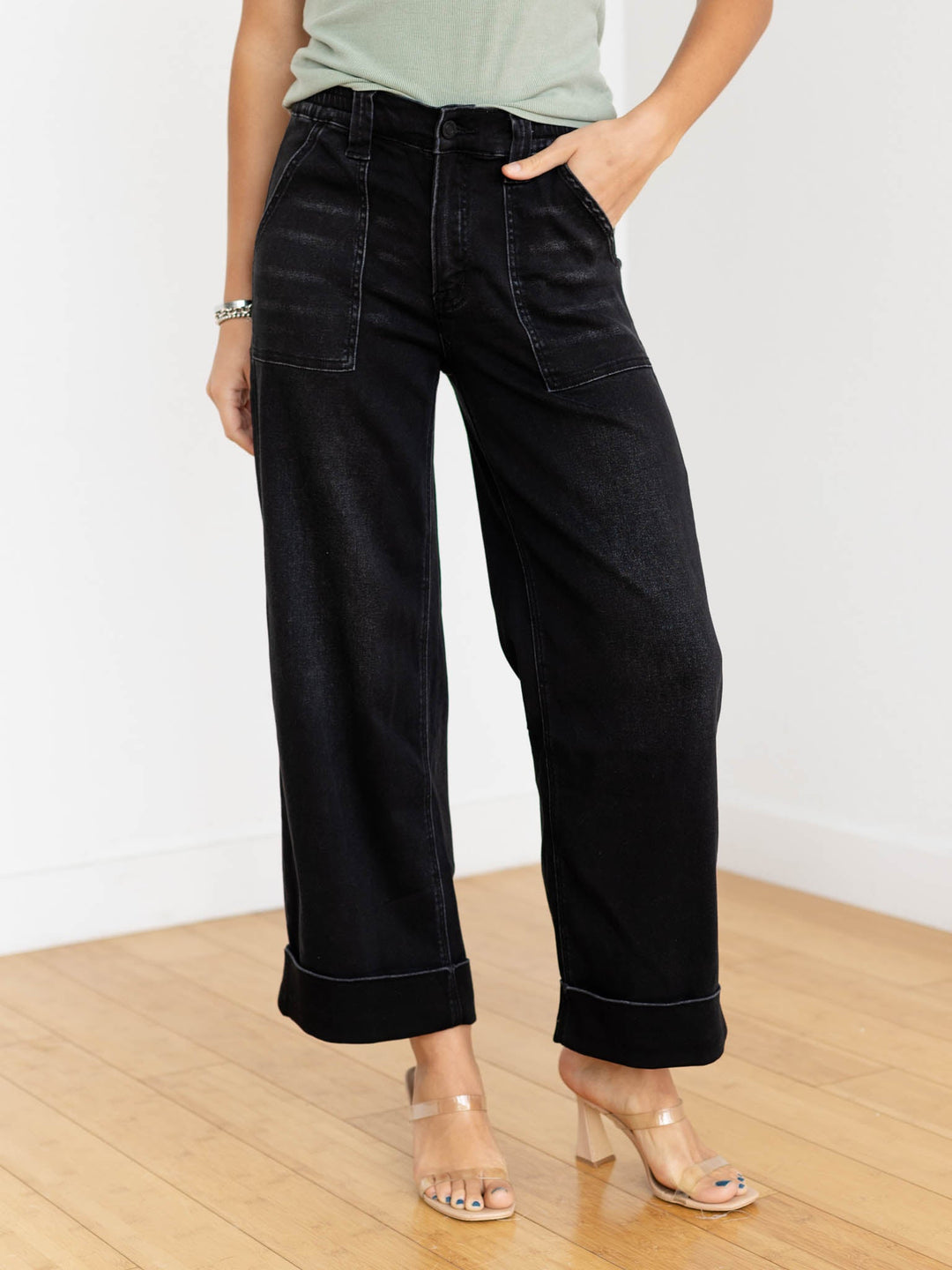 Person wearing black wide-leg jeans on a wooden floor with a white background