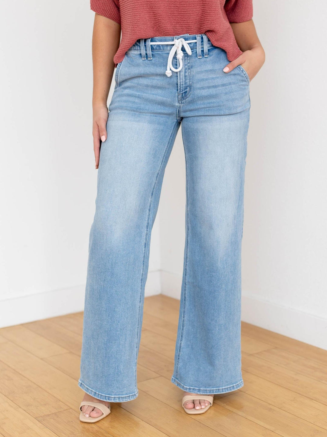 Woman wearing a rust-colored top and light blue jeans on a white background