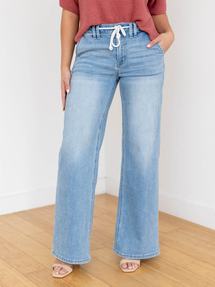 Woman wearing a rust-colored top and light blue jeans on a white background