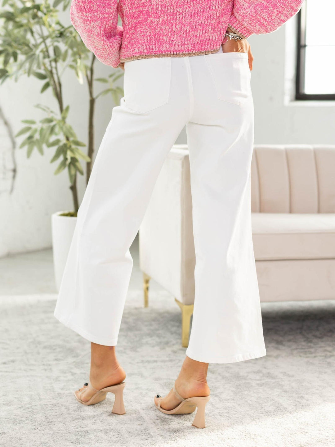 Person wearing white pants and a pink sweater in a room with a plant and sofa.