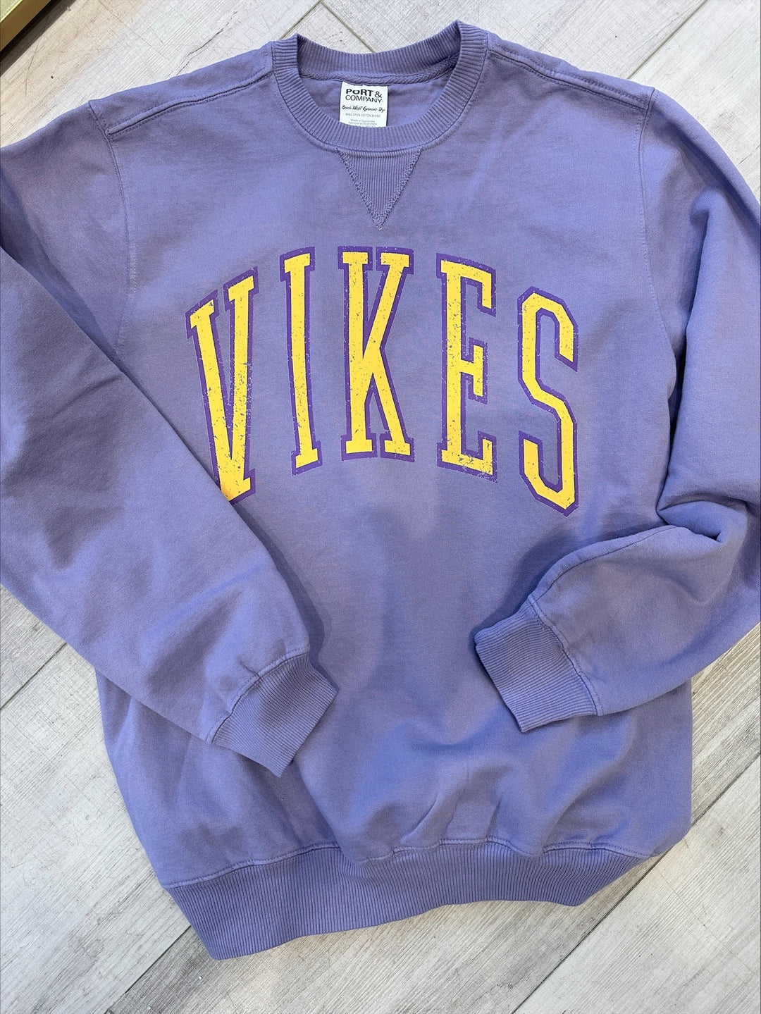 Purple sweatshirt with 'Vikes' printed in yellow on a wooden floor.