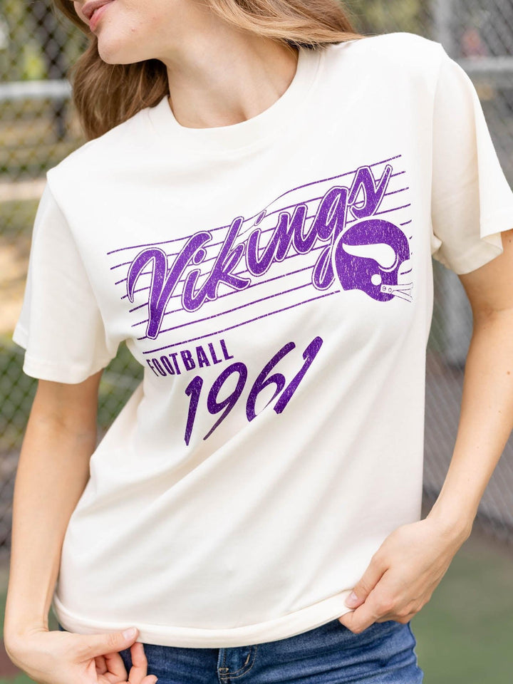 A woman wearing a cream-colored short-sleeve t-shirt with a purple graphic that reads &