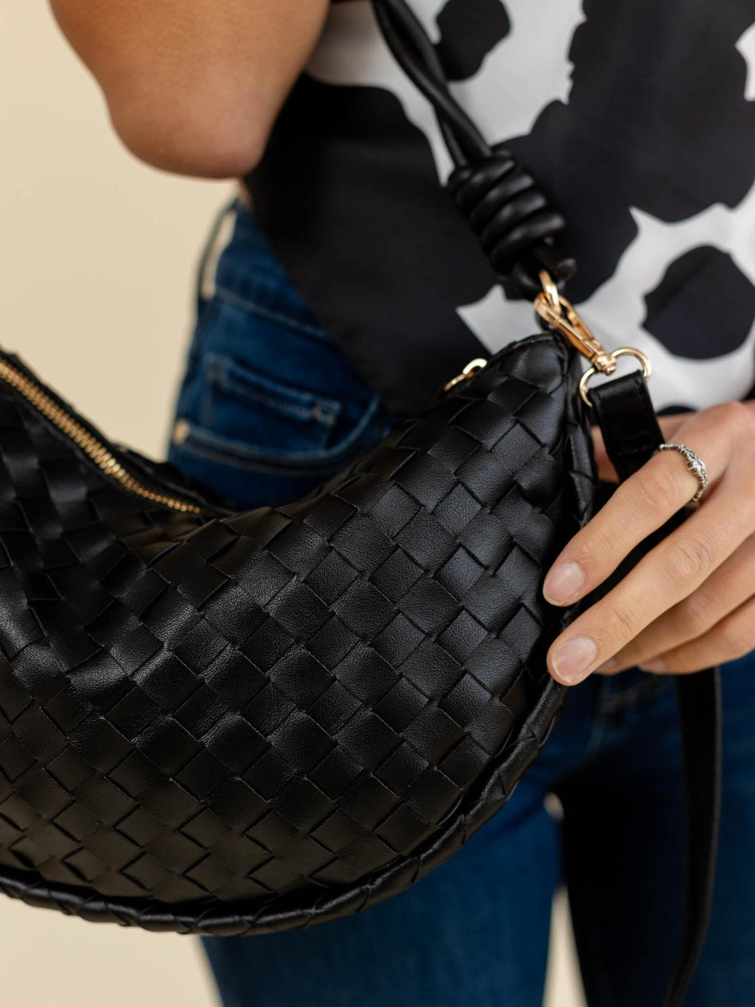 Black woven handbag held by a person with a patterned background