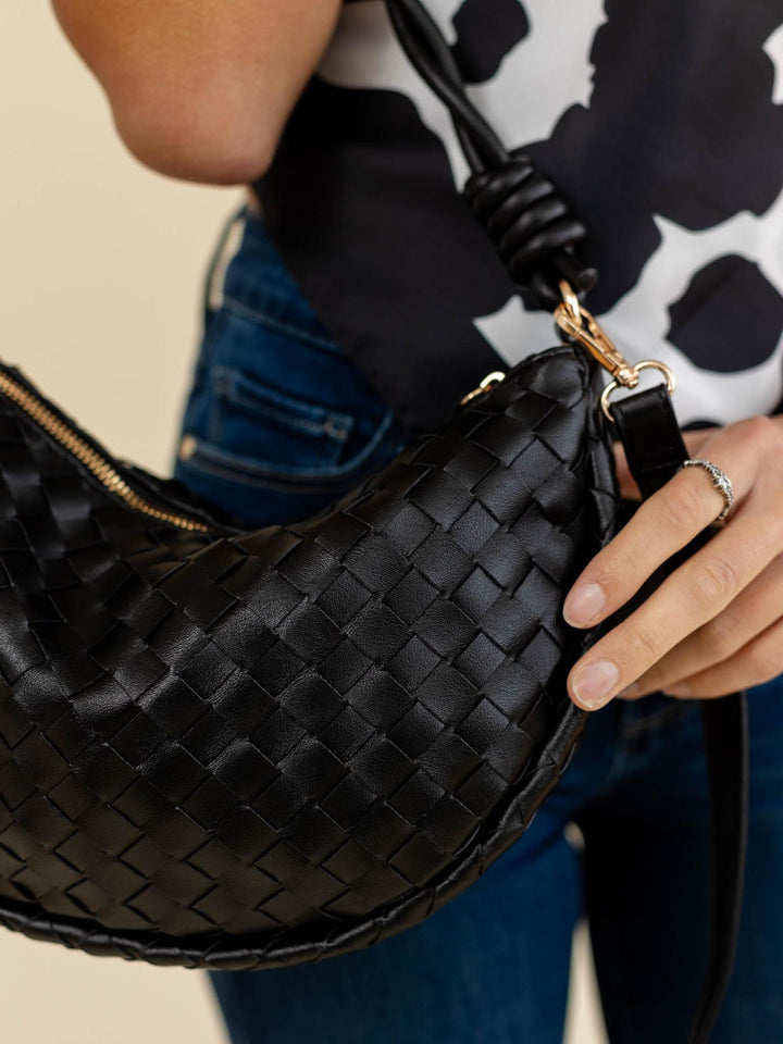 Black woven handbag held by a person with a patterned background