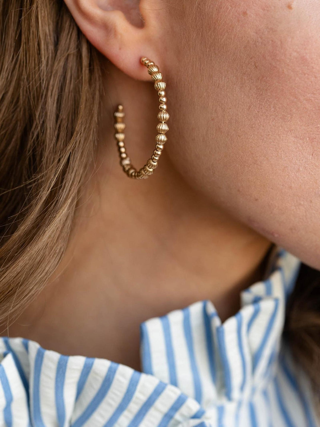 Close-up of a person wearing gold hoop earrings with a striped shirt.