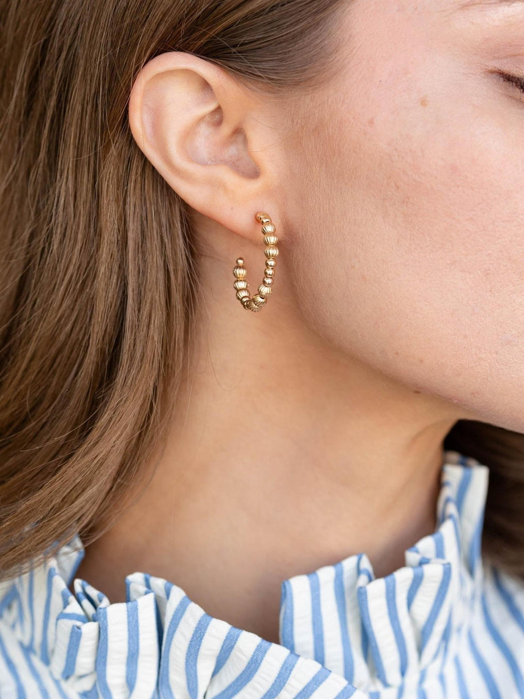 Close-up of a person wearing gold hoop earrings with a striped shirt.