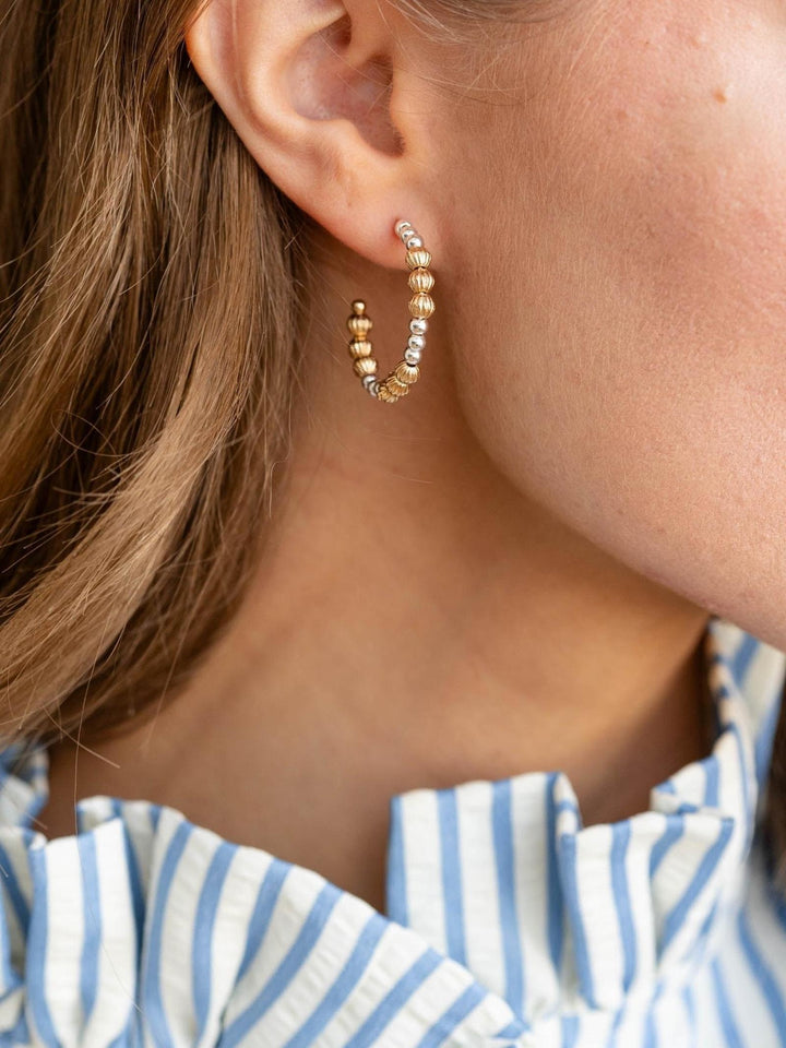 Close-up of an ear wearing a beaded hoop earring with a person wearing a striped shirt.
