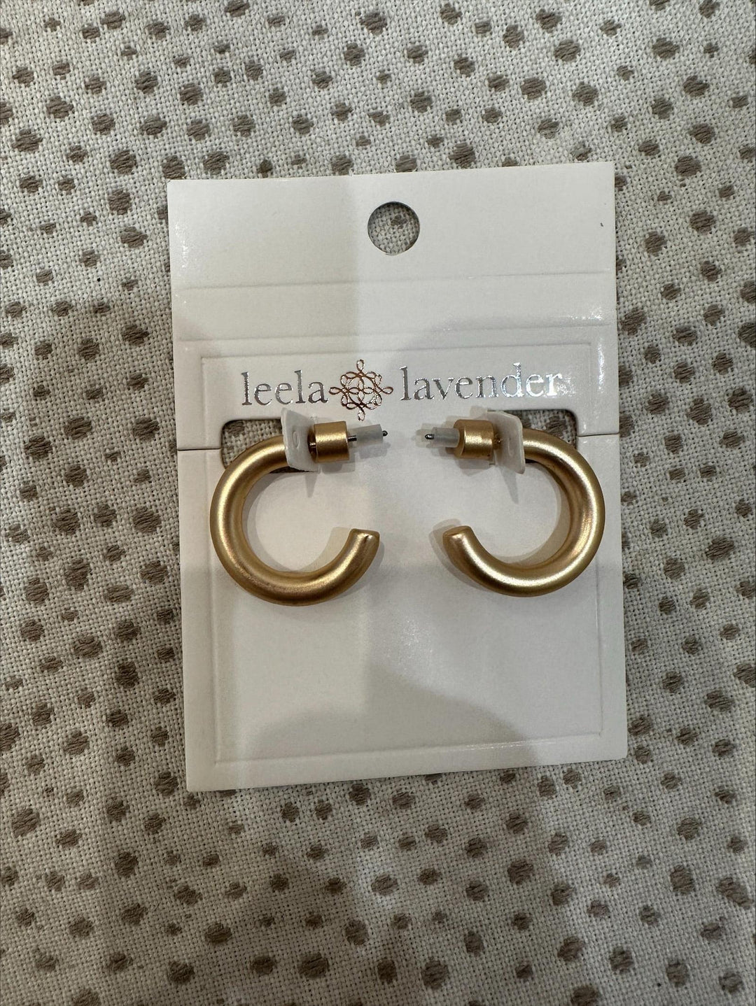 Gold hoop earrings on a Leela Lavender branded card against a textured background