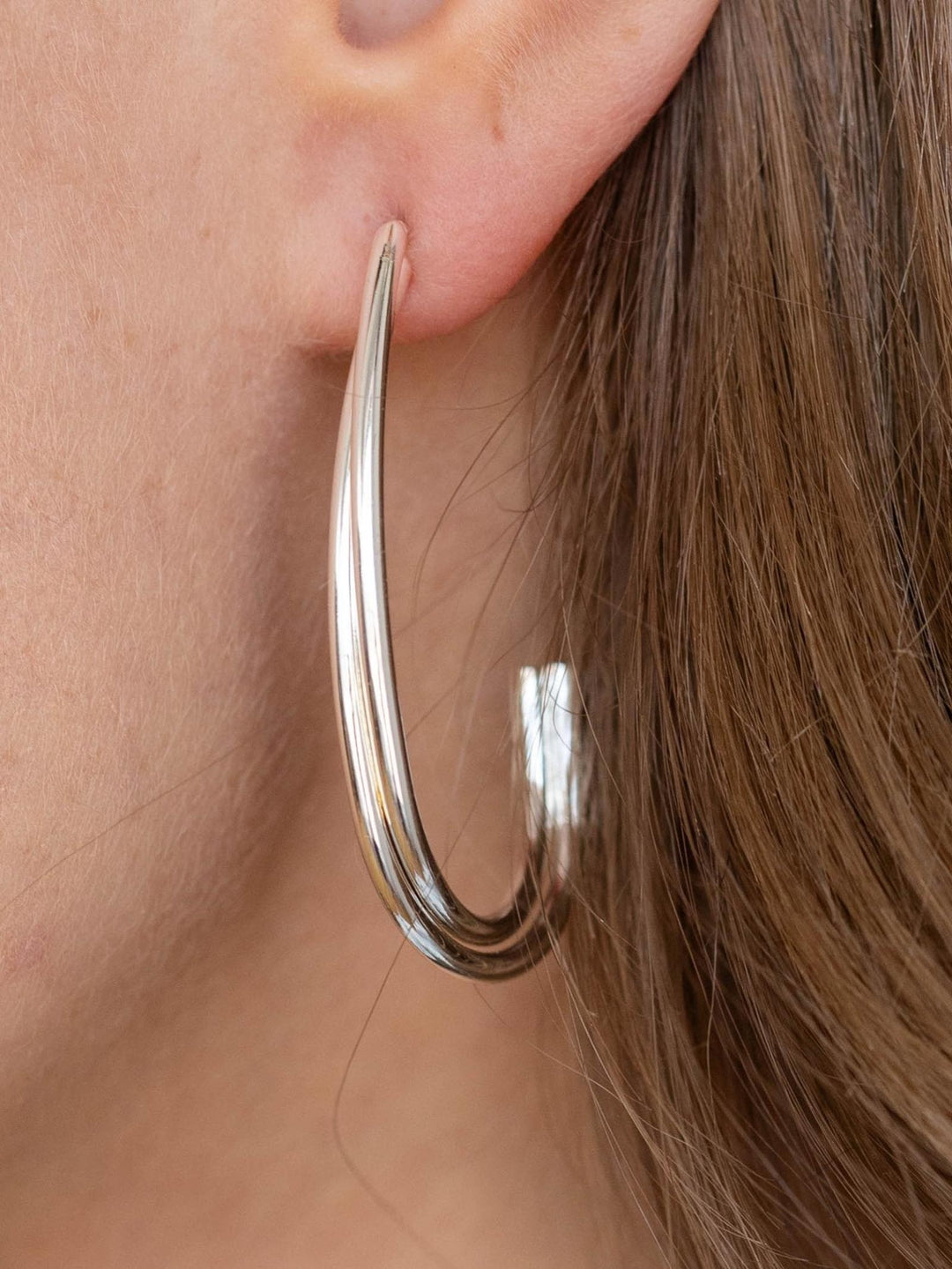 Silver hoop earring worn by a person with brown hair.