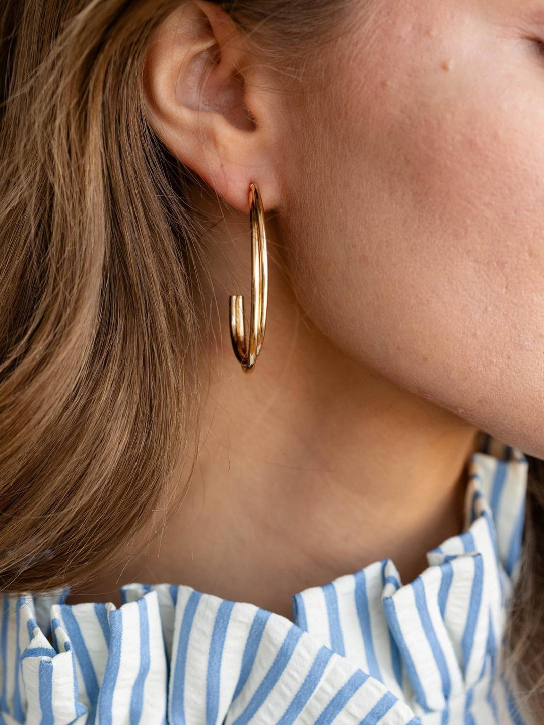 Close-up of a person wearing gold hoop earrings with a blurred background