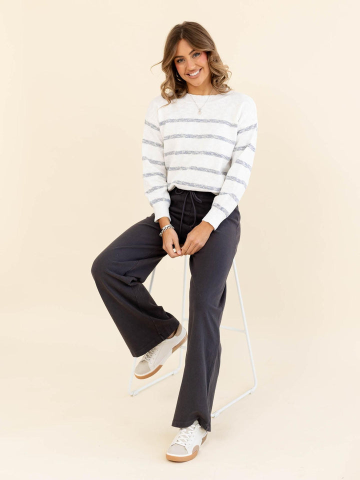Woman wearing a striped sweater and dark pants sitting on a chair against a beige background