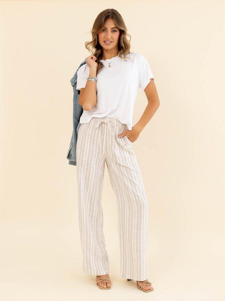 Woman wearing a white t-shirt and striped pants against a beige background