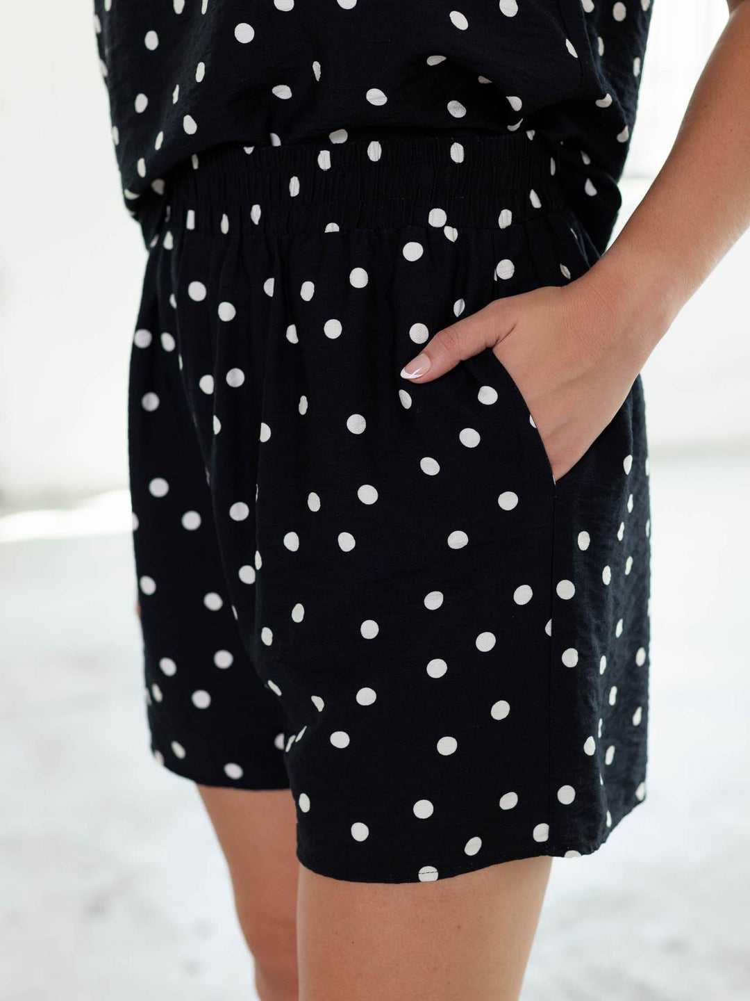 Navy and white polka dot woven shorts with an elastic waistband and a hand in the pocket.