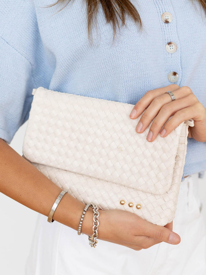 White textured clutch held by a person wearing a light blue sweater.