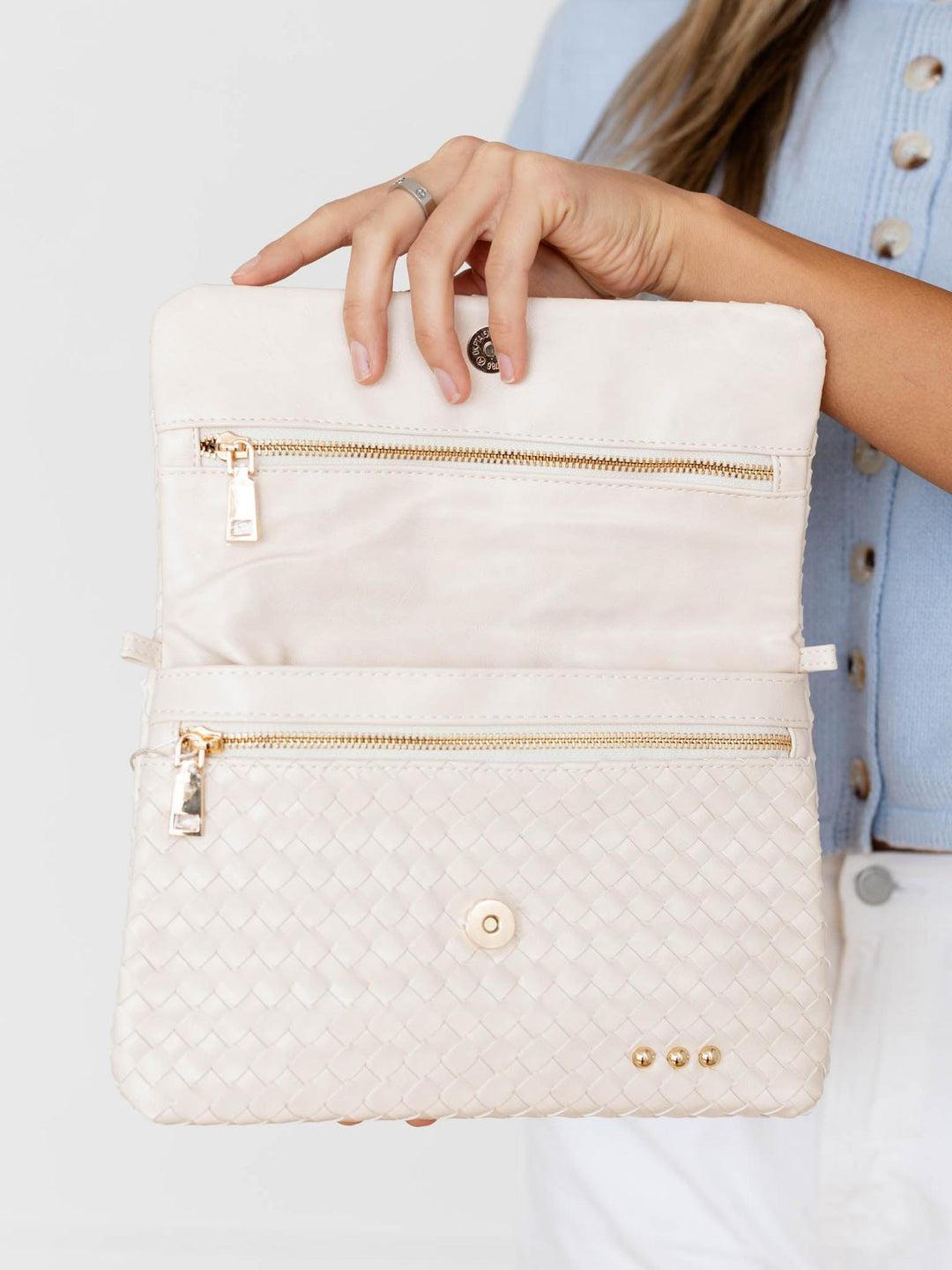 White quilted handbag with gold zippers held by a person wearing a light blue jacket.