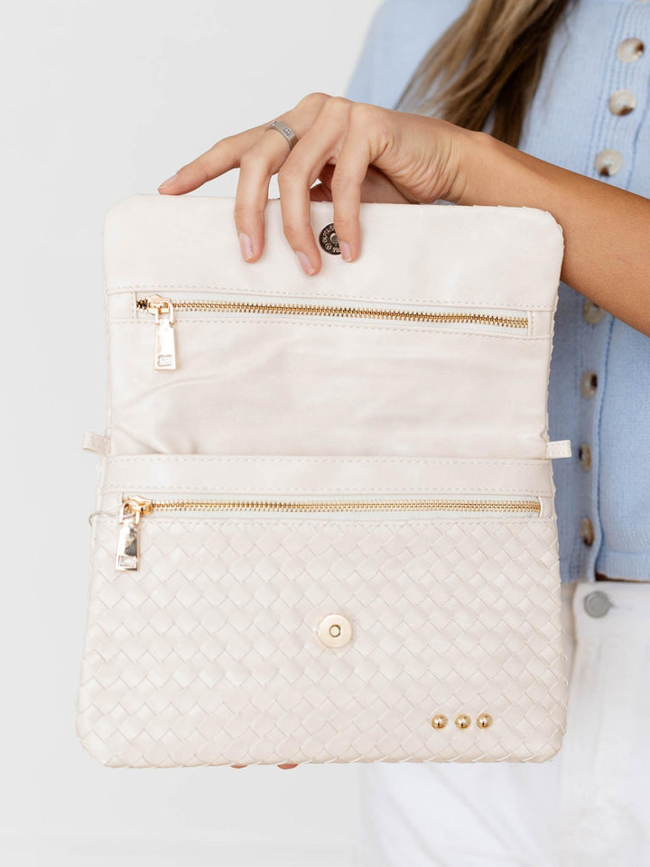 White quilted handbag with gold zippers held by a person wearing a light blue jacket.