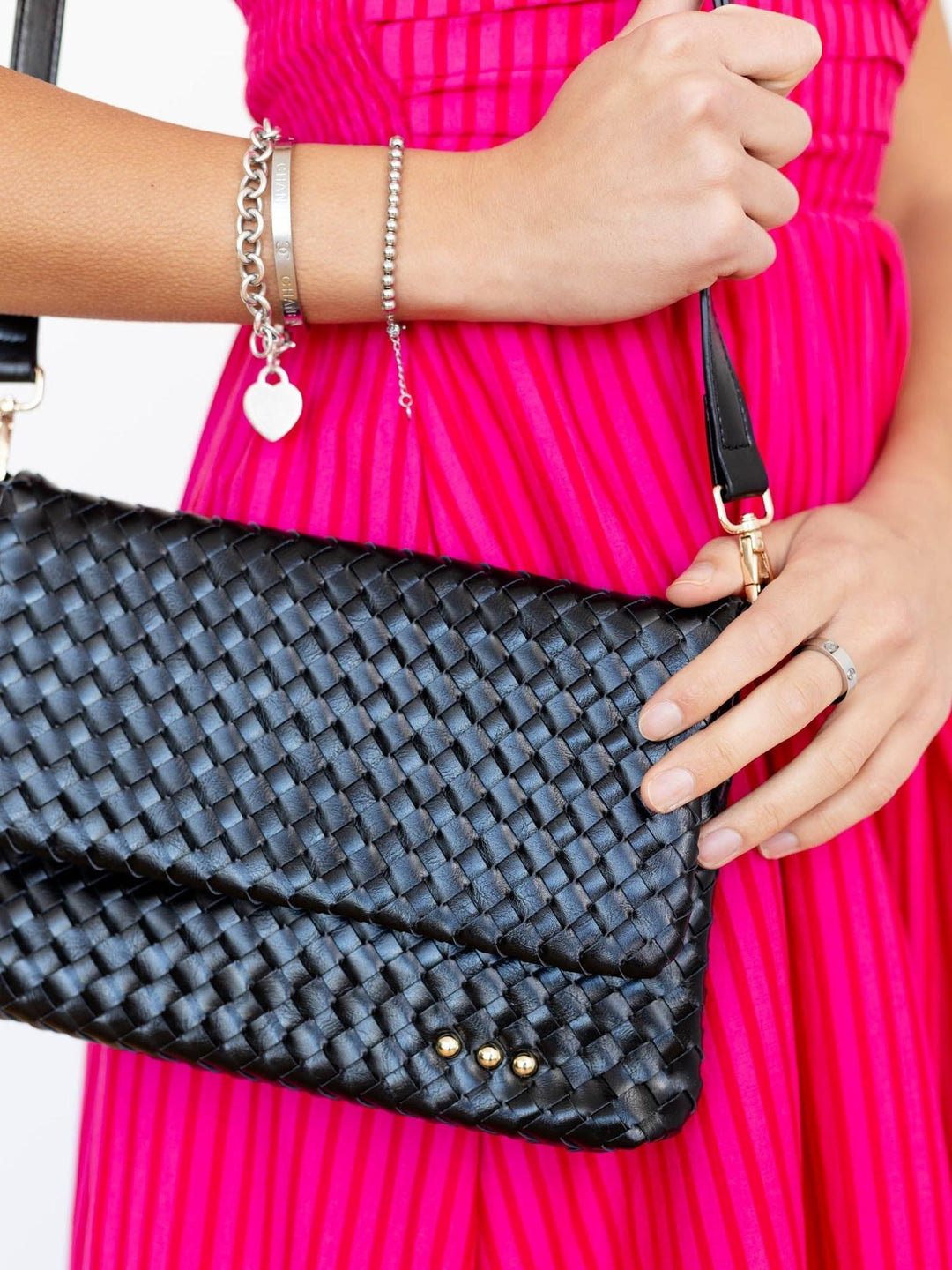 Black woven clutch held by a person wearing a pink dress.