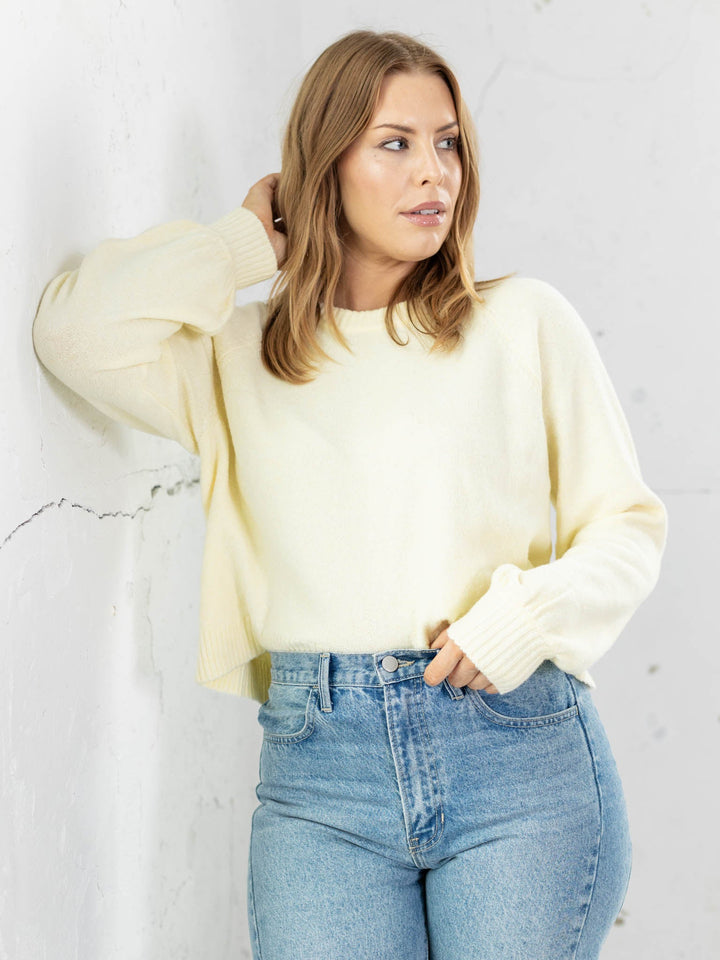 Woman wearing a light yellow sweater and blue jeans against a white background