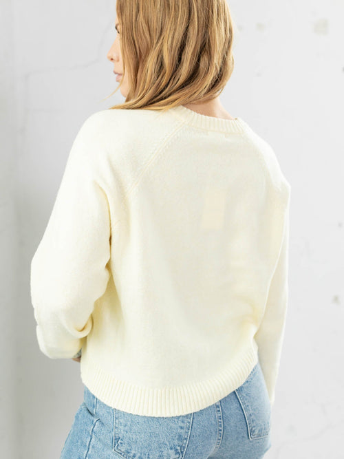 Person wearing a light-colored sweater and blue jeans against a plain background