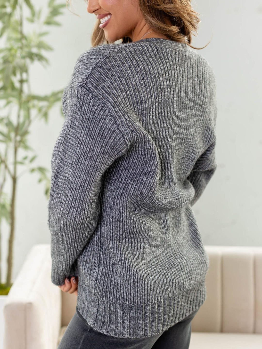 Person wearing a gray sweater in an indoor setting with a plant in the background