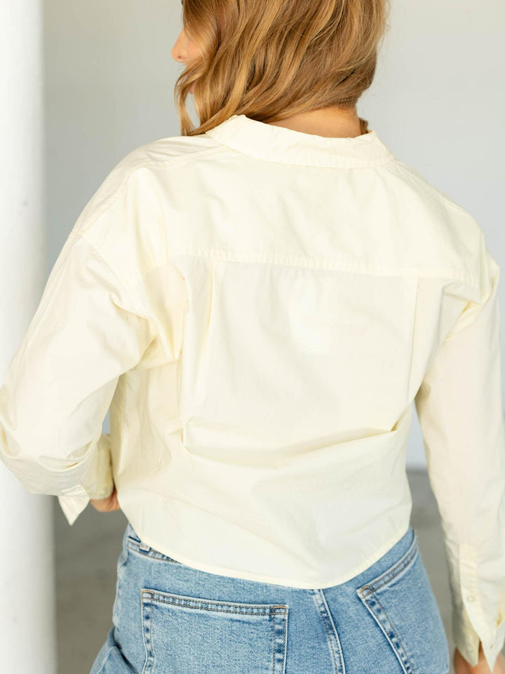 Person wearing a light-colored blouse and blue jeans against a neutral background