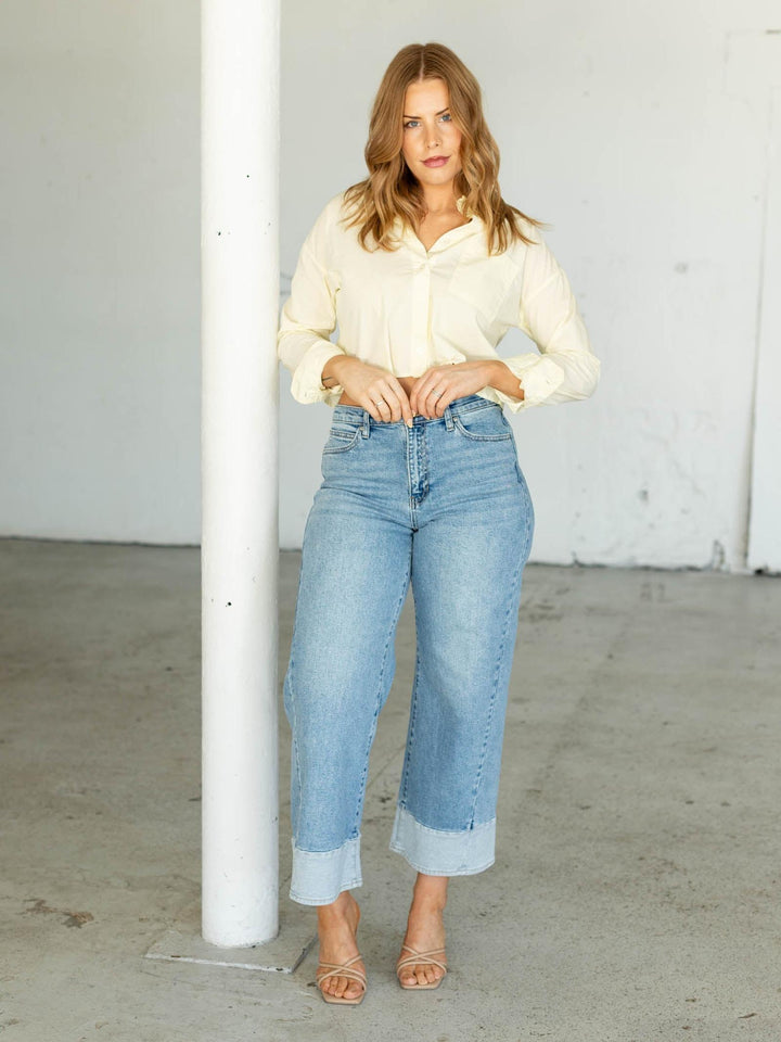 Woman wearing a white blouse and light blue jeans standing against a white wall.
