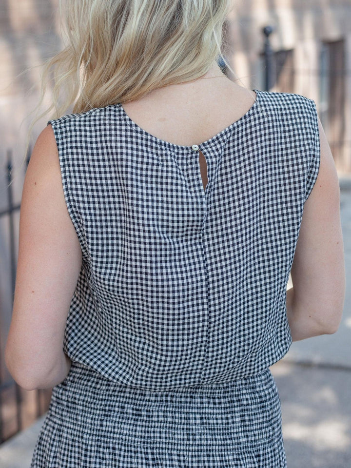 A woman viewed from behind wearing a sleeveless black and white gingham dress, showing the back neckline with a small keyhole cutout.