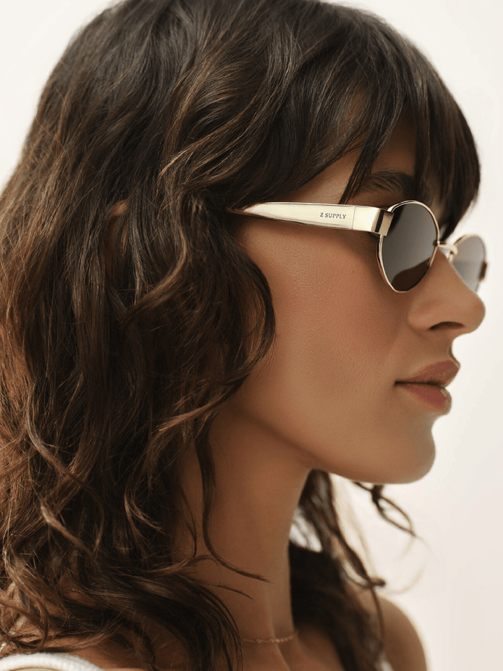 Woman wearing gold-framed sunglasses with a blurred background
