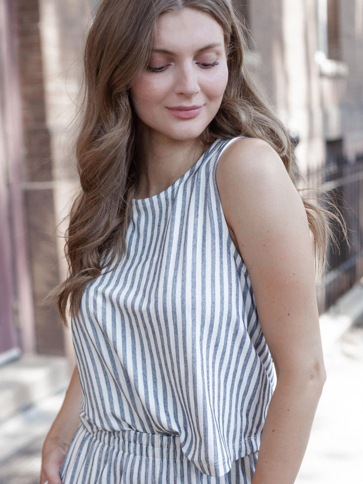 A woman wearing a sleeveless top with vertical navy and off-white stripes, photographed outdoors against a softly blurred urban background.