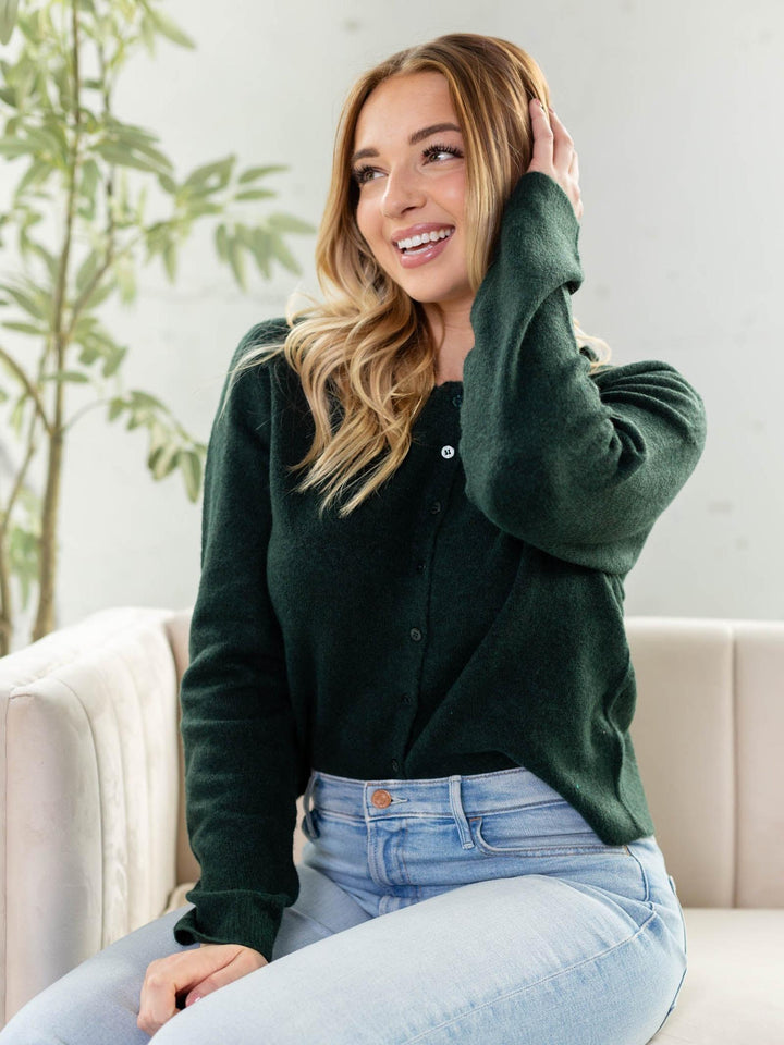 Woman wearing a green cardigan and light blue jeans sitting on a couch.