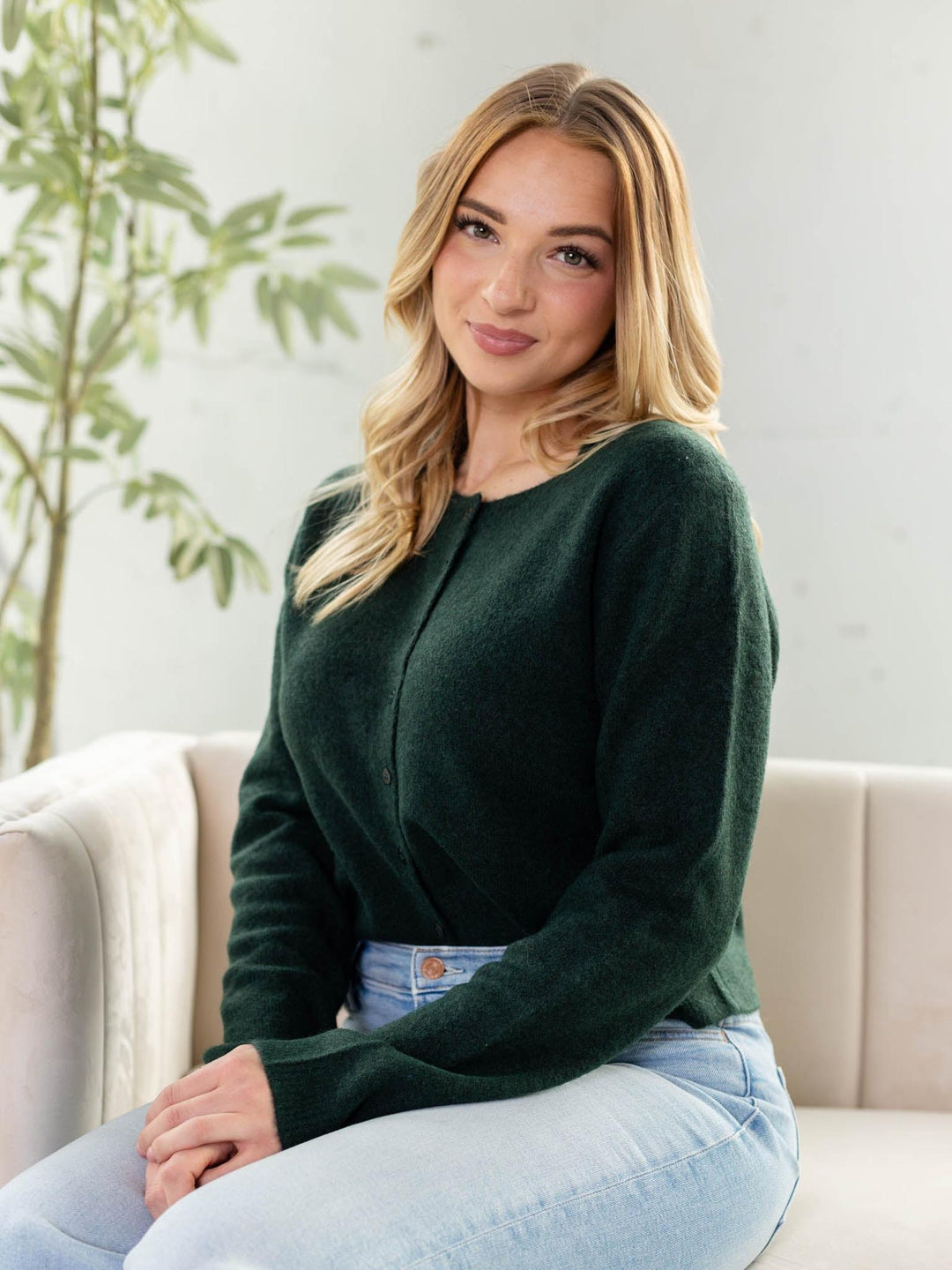 Woman wearing a green sweater sitting on a couch with a plant in the background