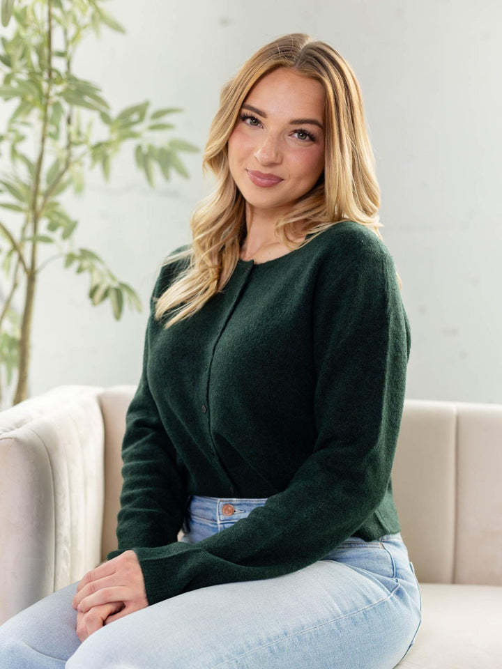 Woman wearing a green sweater sitting on a couch with a plant in the background