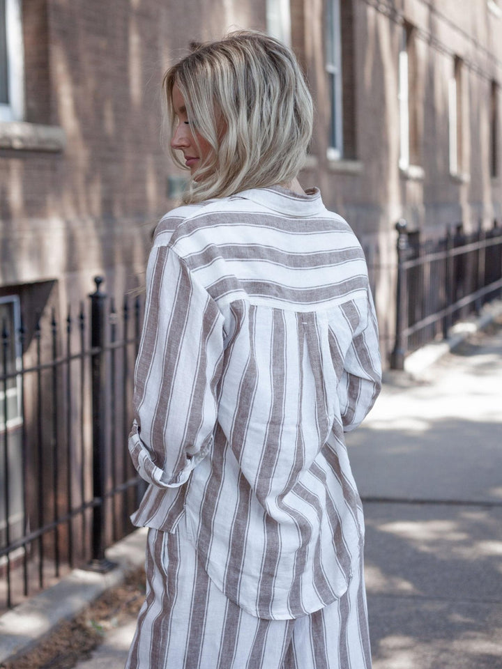 A woman with blonde hair is shown from behind wearing a loose, long-sleeve striped shirt and matching skirt in a city street setting.
