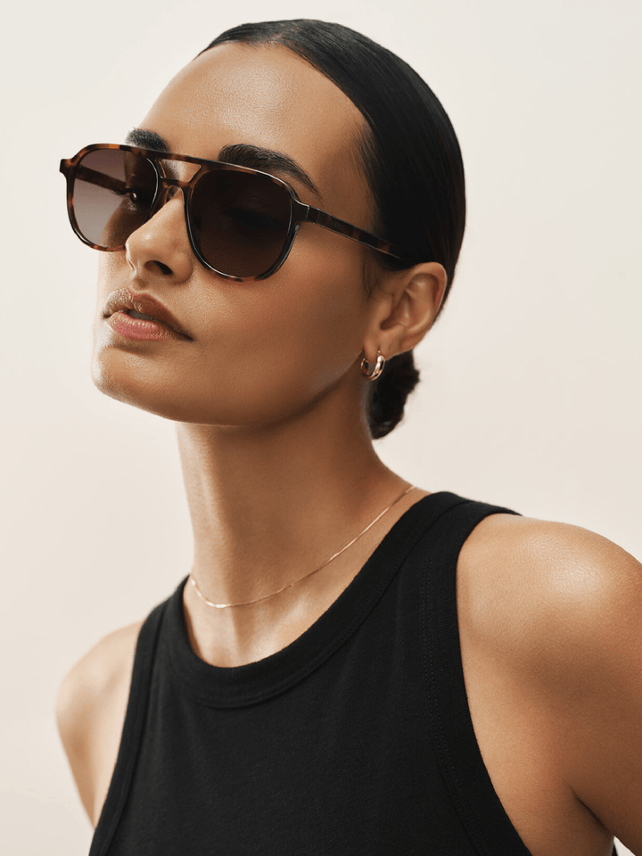 Woman wearing sunglasses and a black tank top against a neutral background