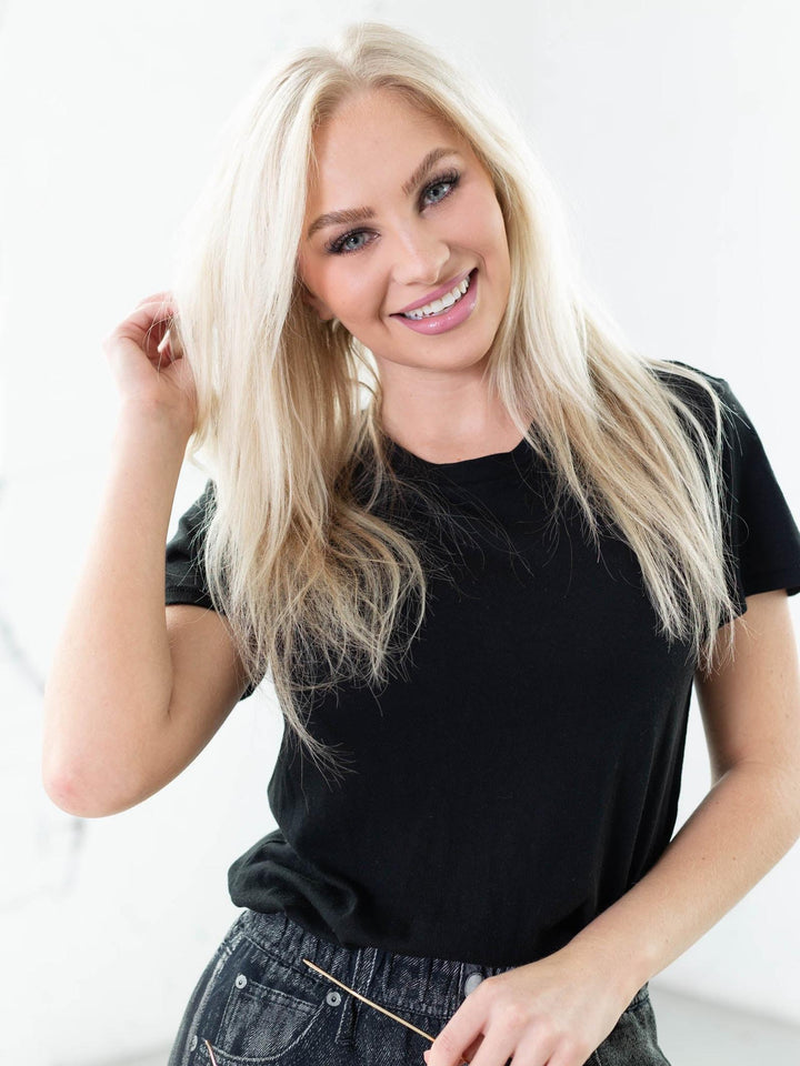 Woman with long blonde hair wearing a black t-shirt against a white background