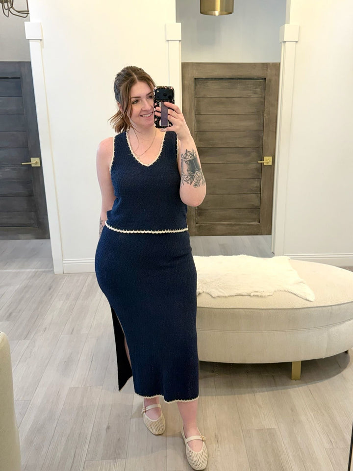 Woman taking a mirror selfie wearing a navy dress in a room with wooden flooring and a white wall.